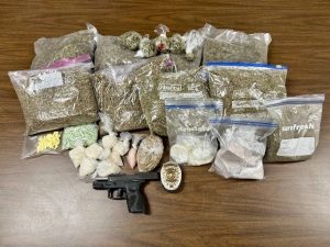 Several packs of drugs lied across a table along with a firearm and a badge.