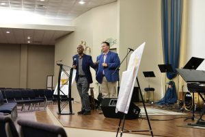 two men in jackets giving presentation with easels on stage 