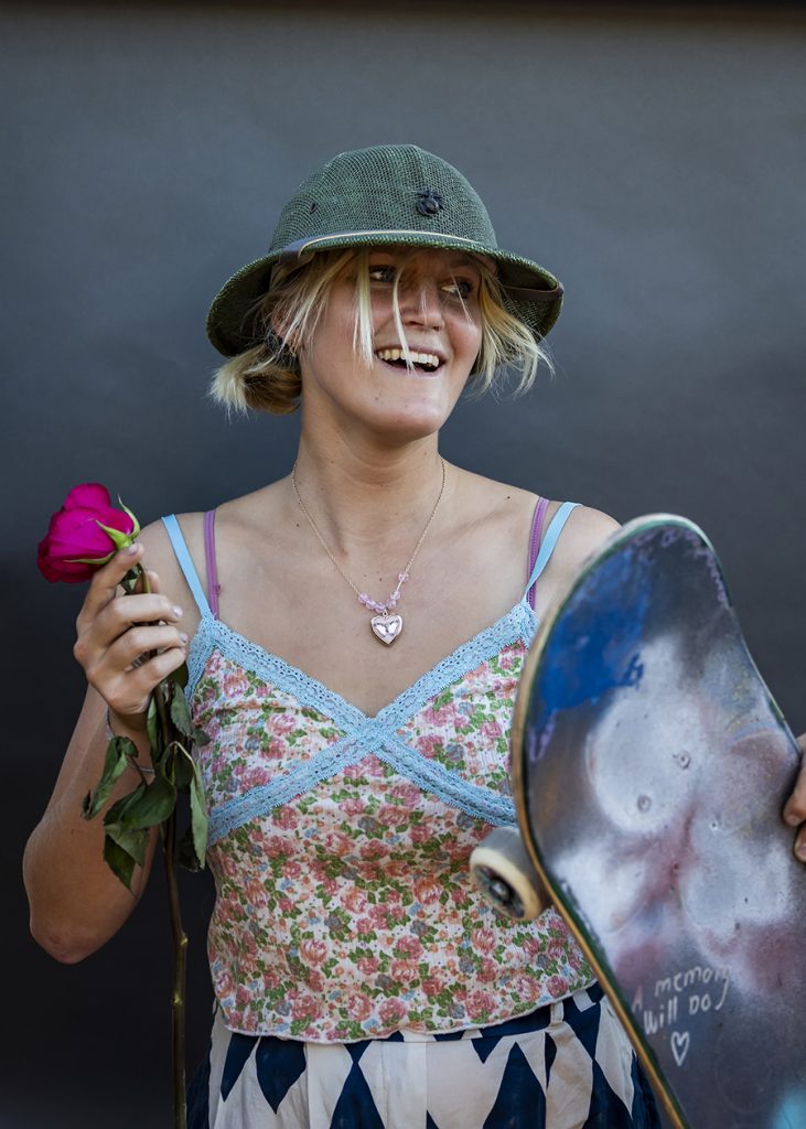 A female skater in a bucket hat holds a rose and a skateboard