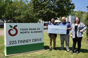 two men on right holding oversized check next to sign for Food Bank of North Alabama