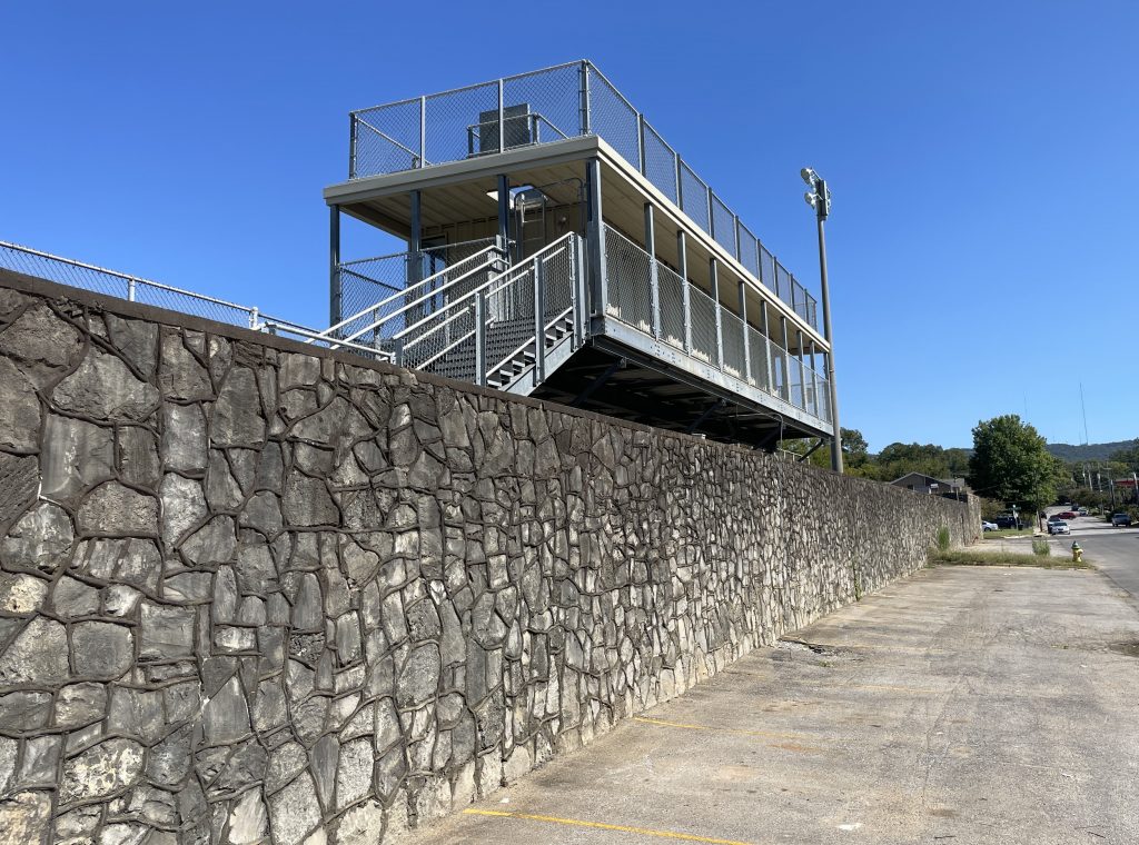 long stone wall with press box style building at top with blue sky in background