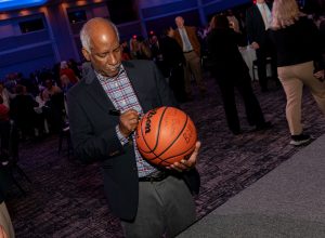 Man in dark jacket and plaid shirt signs orange basketball
