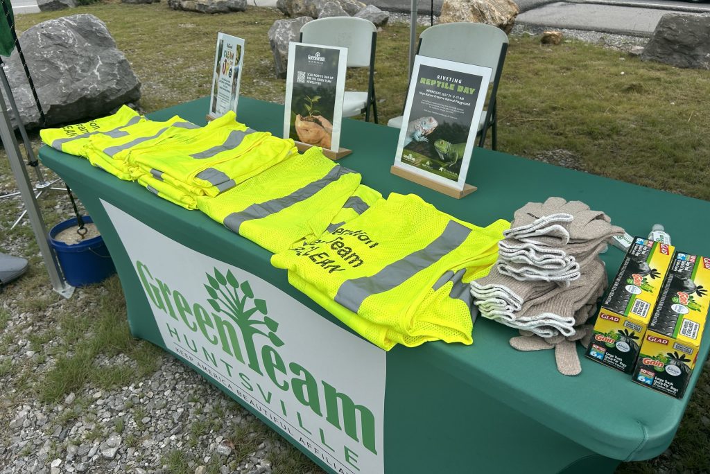 display of litter collecting equipment bright yellow vests, gloves on green table with green team banner on front