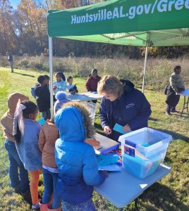 children at outdoor table with adult giving demonstration under green canopy