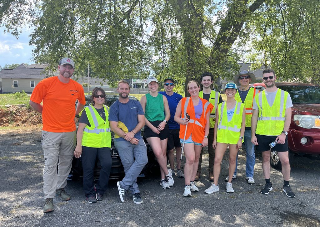 group of people outdoors, some in safety vests, with large tree in background