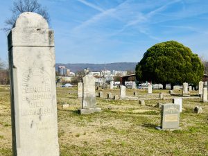 Photo of a headstone in Glenwood Cemtery in the foreground and the City of Huntsville skyline in the background