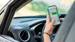 Photo of a person holding a phone, getting ready to send a text, behind the wheel of a car