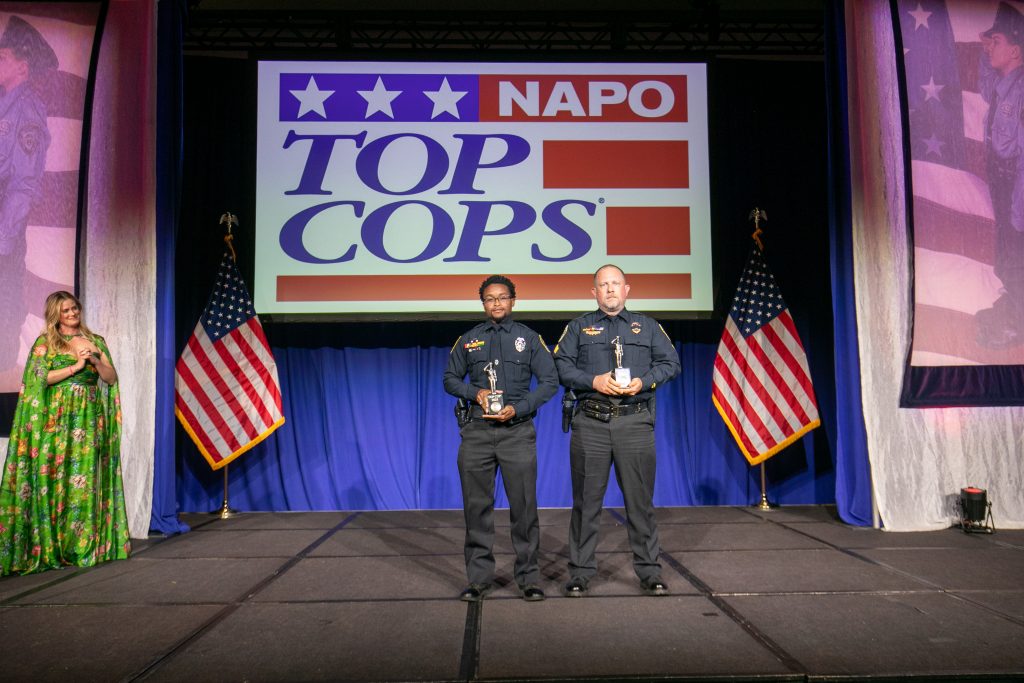 Officer Jason Toney and Sgt. Kevin Lambert pose for photo in front of projector screen at TOP COPS Awards 2025. Photo Courtesy: National Association of Police Organizations