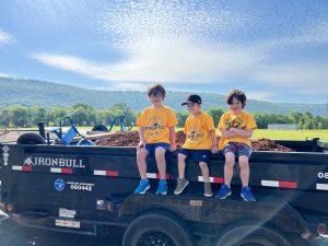three young boys in yellow shirts sitting on trailer carrying mulch