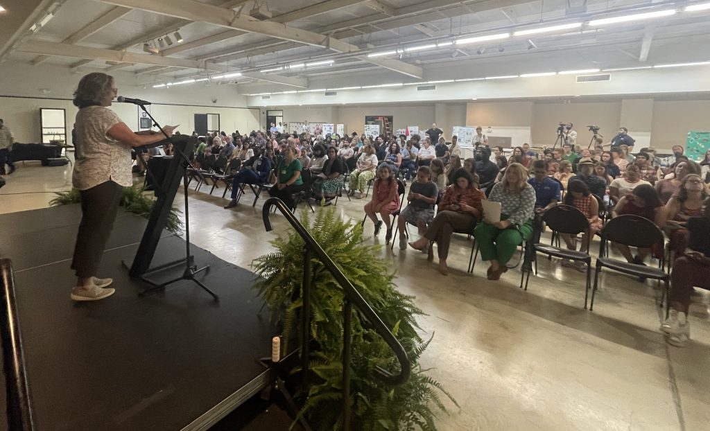 woman speaking into microphone on stage addressing large crowd of students