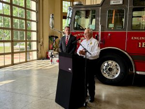 man in white shirt speaks at podium with fire truck in background