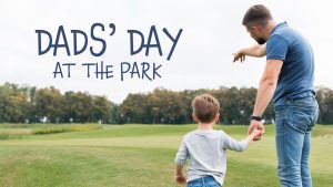 child holding his father's hand while walking onto a ball field