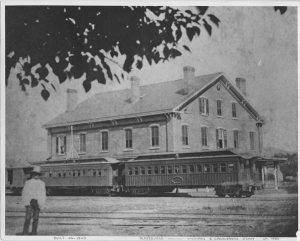 black and white photo of a man standing in front of a train station