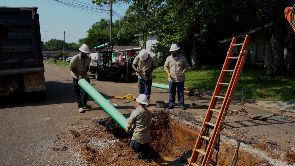 construction workers lowering green pipe into work area in road