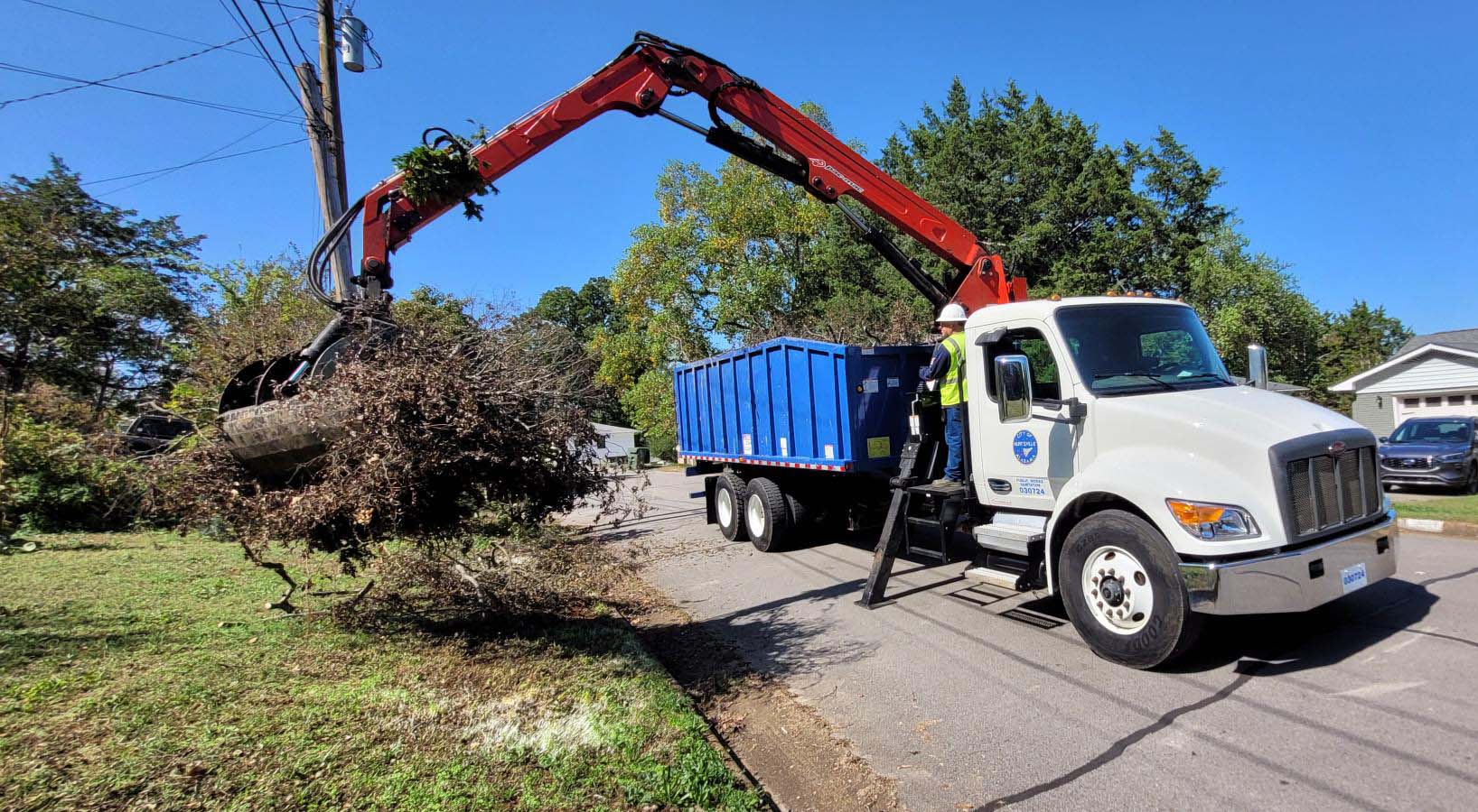 large city boom garbage truck pick up tree limbs and debris on the side of the road