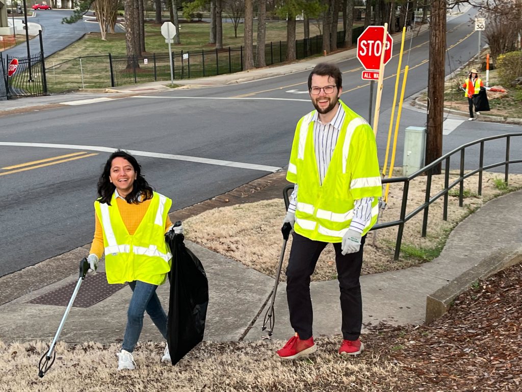 woman and man wearing safety vests and collecting litter along roadside