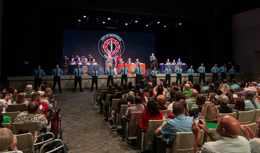 group of graduating firefighters in blue shirts standing before audience