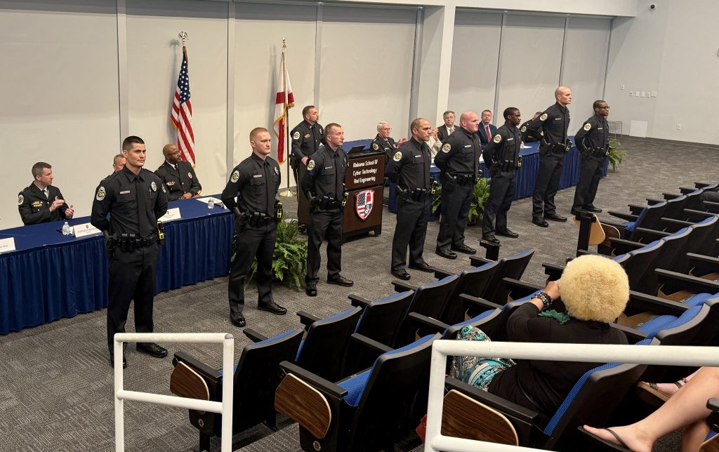 graduate class of police officers in uniform standing in front of audience