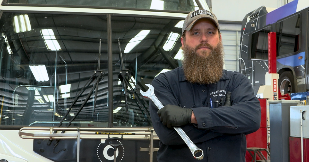 White male mechanic holding wrench standing in front of Huntsville Transit bus
