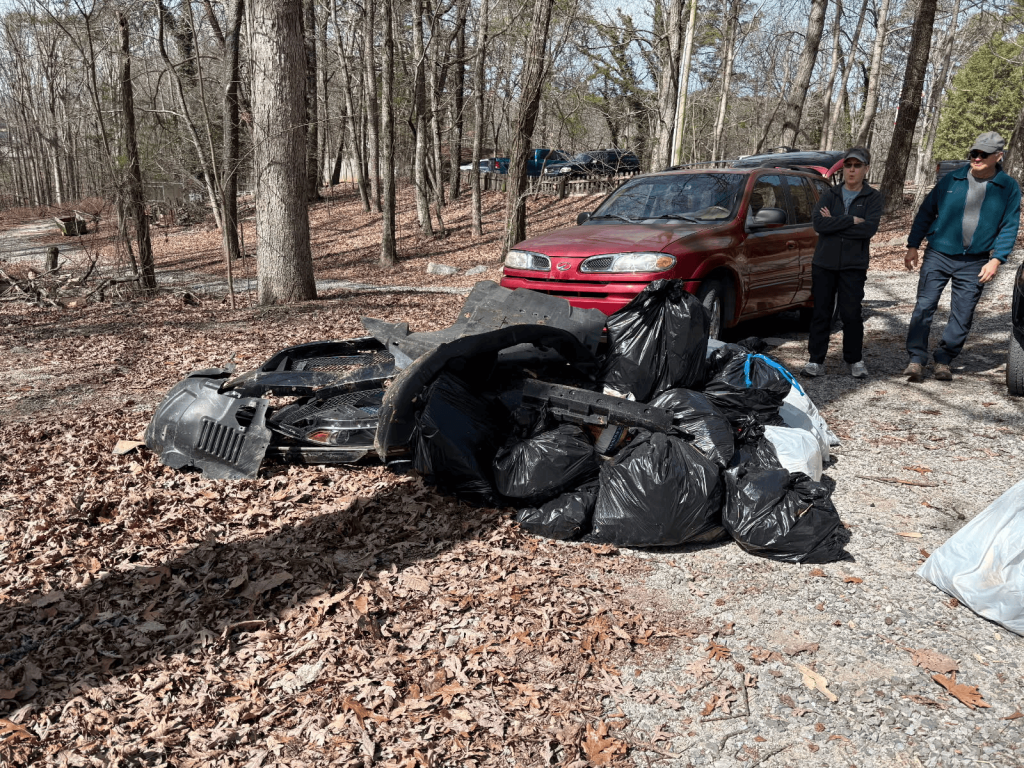 bags of litter in wooded area with red vehicle in background