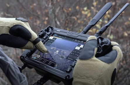 A person holding a small, digital tablet with antennas. The screen is a controller for an unmanned aerial vehicle, also known as a drone.