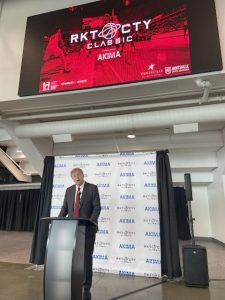 Mayor Battle speaks from a podium in front of a Rocket City Classic - Akima sign