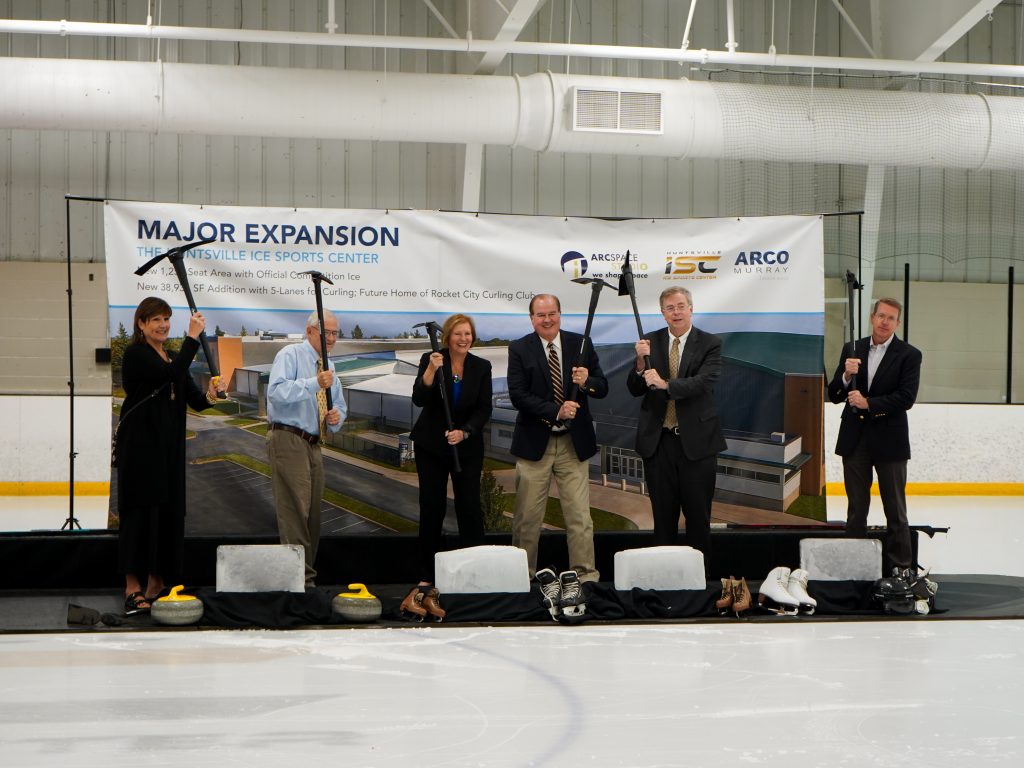 Three men and two women holding pickaxes over their heads readying to break some large ice blocks during a ribbon cutting