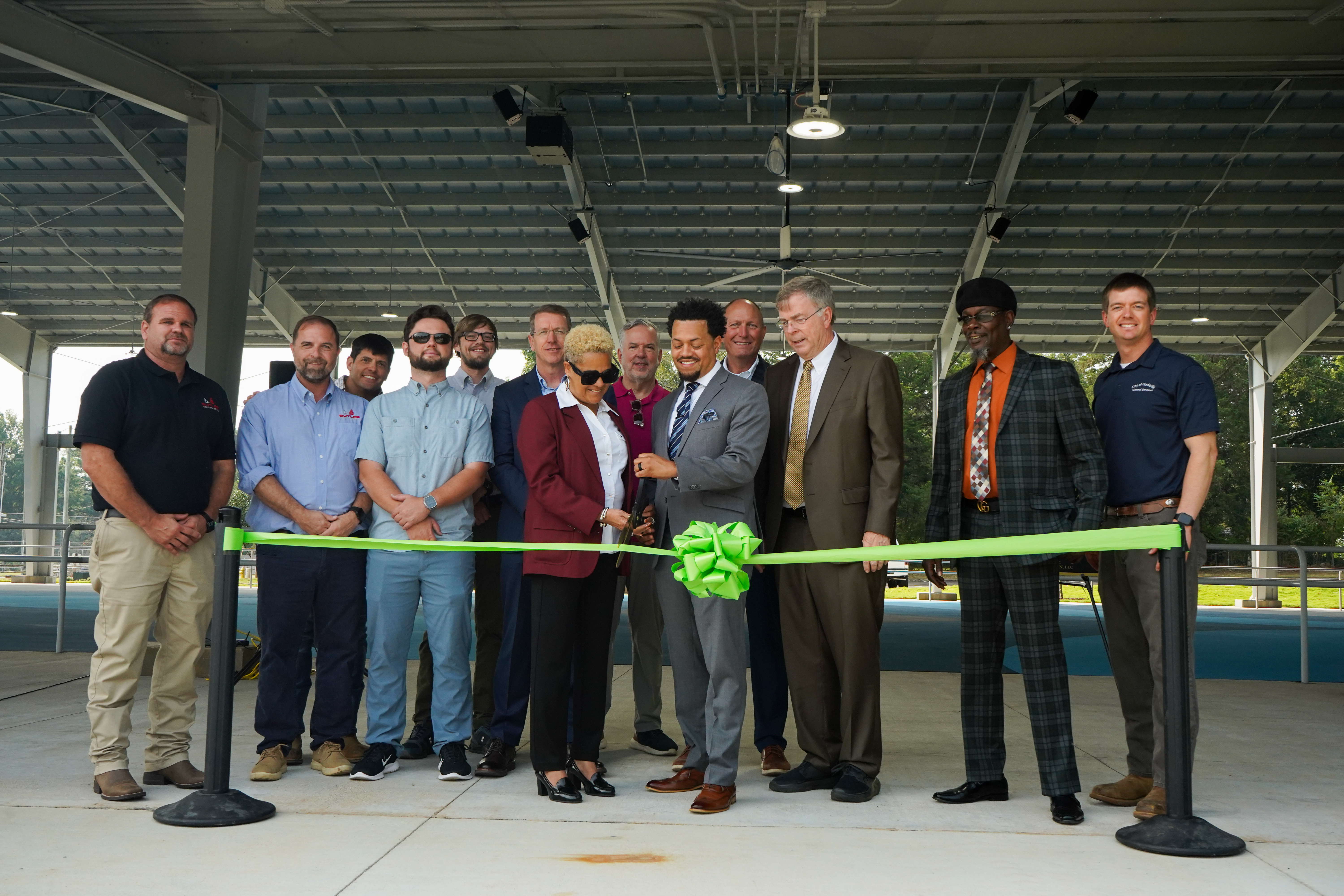 A group of City of Huntsville leaders, contactors and architects, community members and city employees stand under the pavilion of the new Stoner Park Skating Rink to cut the ribbon and open the facility.