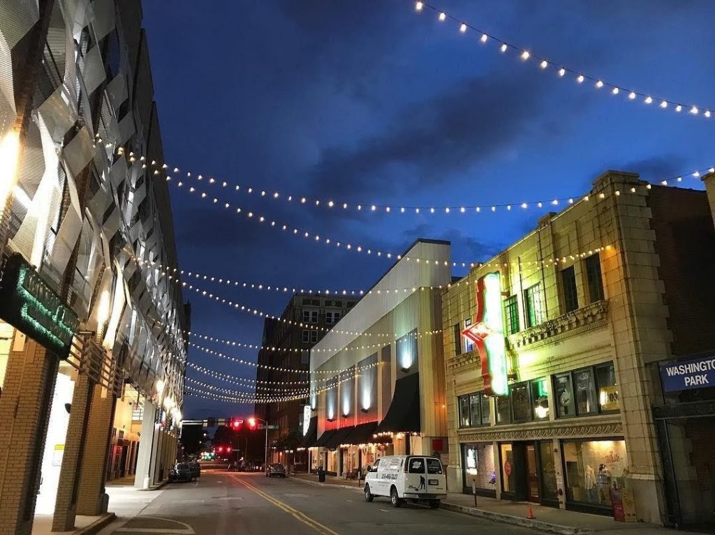 Urban street featuring twinkle lights suspended above retail shops at dusk