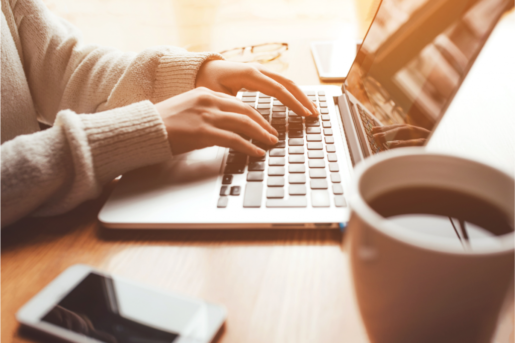 Woman's hands using a laptop computer with a cell phone and cup of coffee off to the side