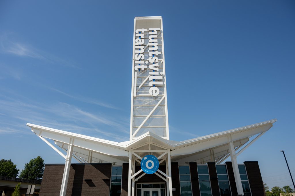 Public transit building with large white sign that says Huntsville Transit...on a bright sunshine day with blue sky