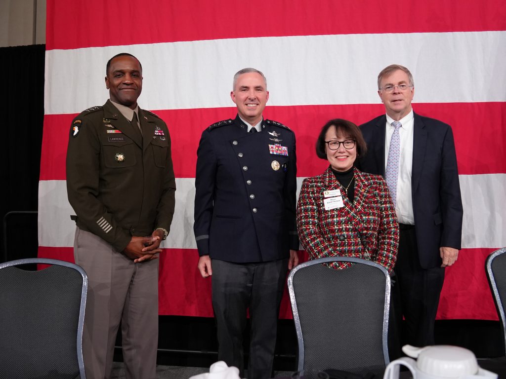 three men and woman pose for photo in front of large flag
