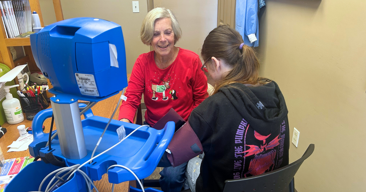 Woman smiling at female patient as she checks her blood pressure in a small triage room