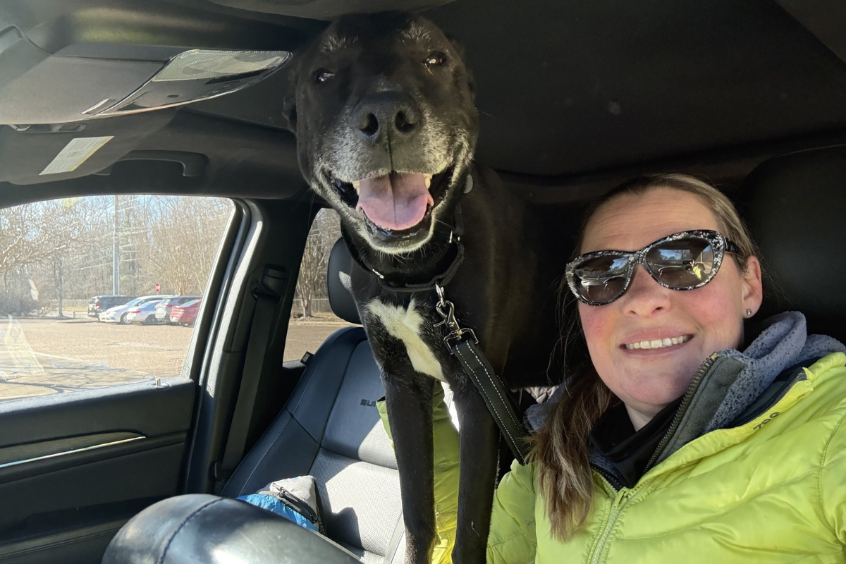 Woman in green jacket holding dog in car