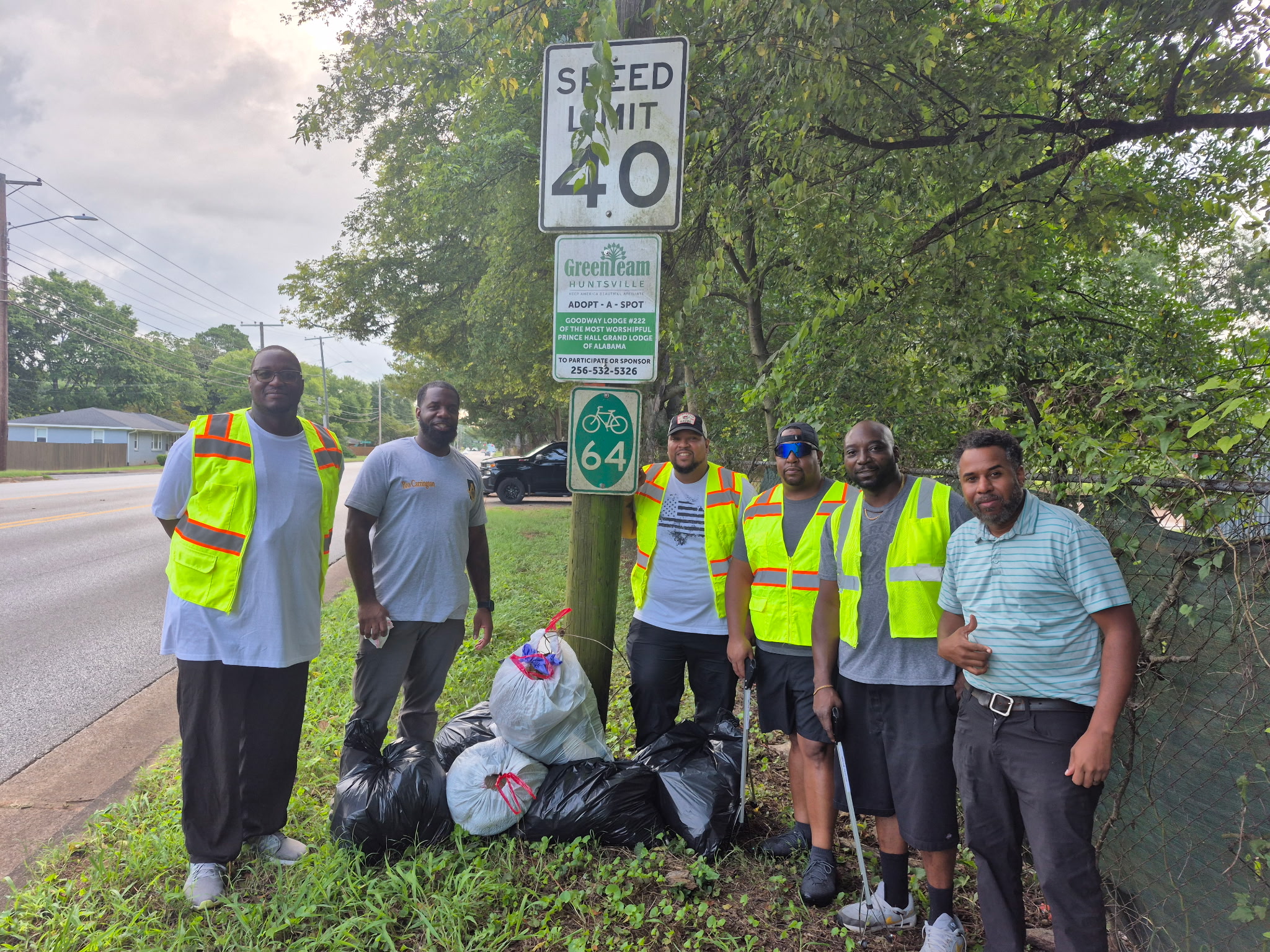 A group of six men wearing bright green vests volunteer to pick up litter along Oakwood Avenue