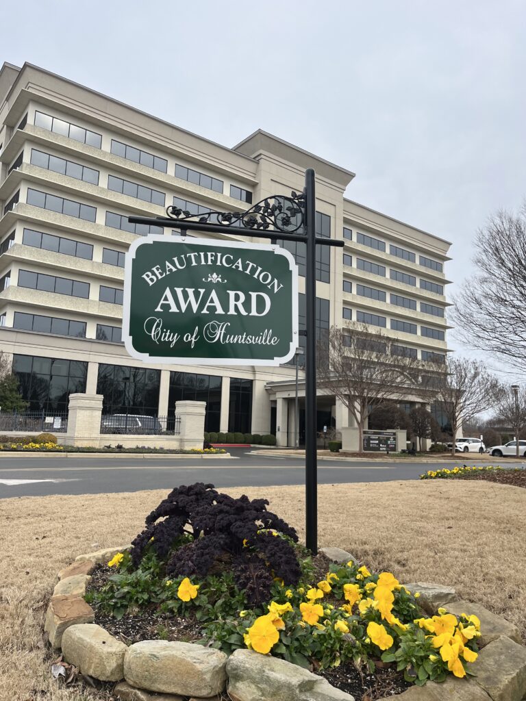 City of Huntsville Beautification Award sign on a post in the ground, surrounded by pretty flowers and foliage.