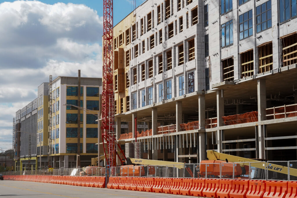 Construction site of large building with a crane in front and orange traffic barricades