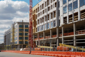 Construction site of large building with a crane in front and orange traffic barricades
