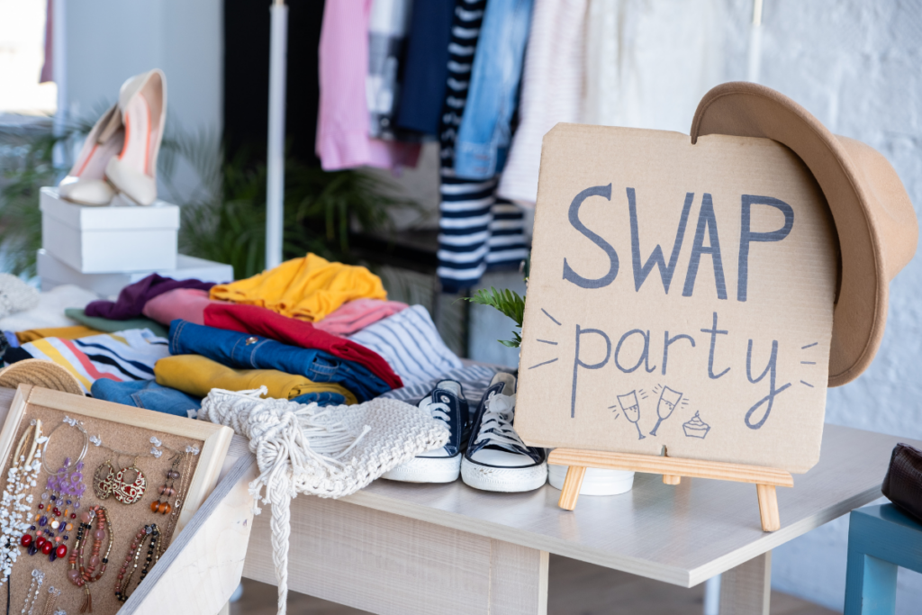 A photo of shoes, clothes, scarves, hats and jewelry that are part of a clothing and accessories neighborhood swap party. There also is a handwritten sign on cardboard that says Swap Party.