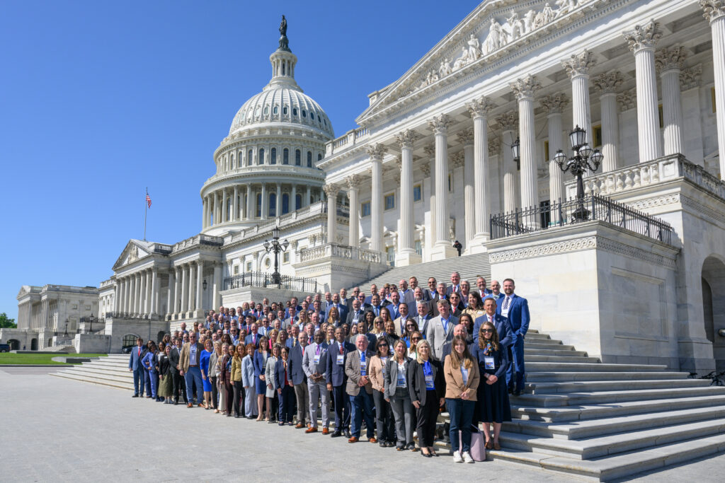 A very large group of about 200 people pose on the steps of the U.S. Capitol with the Capitol dome in the background.
