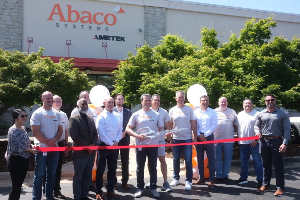 group of people lined up at ribbon cutting outside abaco systems building