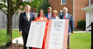 Five people stand outside holding large signs. The signs celebrate Huntsville, America's 250th anniversary and feature the Meta logo.