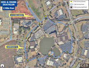 A detailed aerial map shows the 2‑mile running route for the Heel & Crank Duathlon. The path is marked with a blue line and yellow arrows indicating the running direction. The route loops around buildings, parking lots, and a central pond, passing along streets labeled Mark C. Smith Drive, Discovery Drive, and Explorer Boulevard. A star icon marks the start and finish point near the bottom of the map. A legend in the top right corner identifies route symbols, and a GIS City of Huntsville logo appears in the lower right corner.