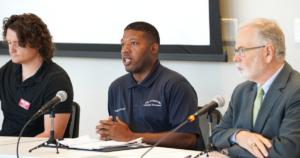 Three people sit at a table with microphones in front of them, participating in a media roundtable discussion.