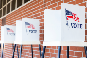 Three voting booths set up outside against a brick wall.