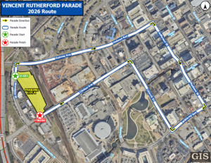 An aerial map displays the 2026 parade route for the Vincent Rutherford Parade. The route is marked with a blue line and yellow arrows showing the parade direction. The parade starts on Woodson Street near a green‑labeled start point beside Parking Lot K, then travels along Holmes Avenue, Jefferson Street, Monroe Street, Williams Avenue, Madison Street, and Clinton Avenue. The route loops back toward the finish point marked with a red star located near the bottom left of the map. A legend explains symbols for parade direction, route, start, and finish. Various city streets, buildings, parking areas, and green spaces are visible throughout the map, with a GIS City of Huntsville logo in the lower right corner.
