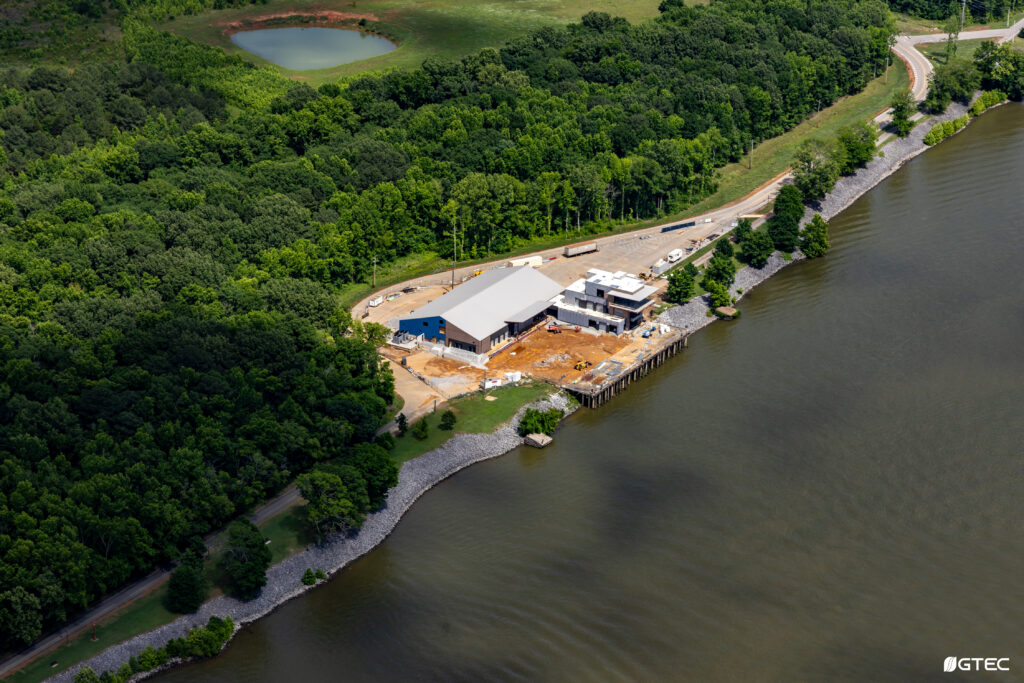 aerial view of under-construction event center surrounded by trees and river on right