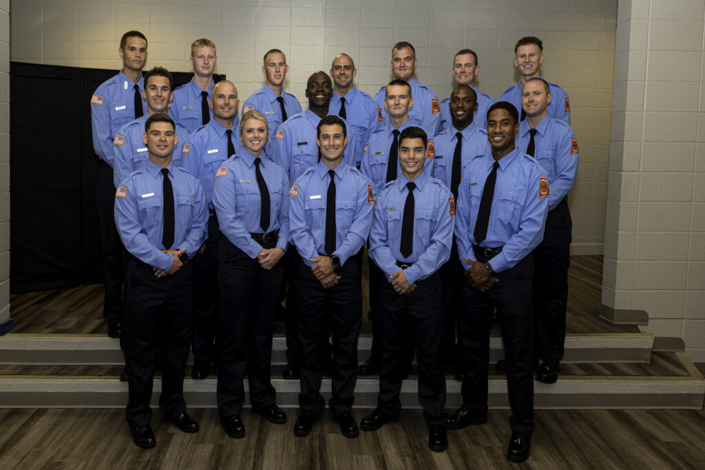 group of 18 firefighters in blue shirts posing for photo at graduation