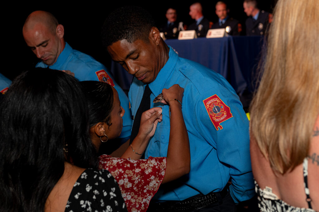 firefighter in blue shirt at graduation getting badge pinned on uniform