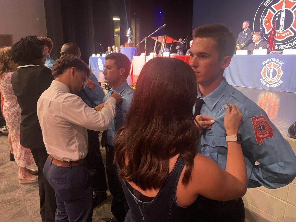 several firefighters in blue shirts having badges pinned on their uniform by family
